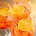 Vista de cima de três taças de Aperol Spritz com gelo e rodelas de laranja flutuando, dispostas em uma superfície rústica.