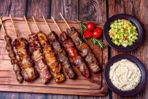 Espetinhos de carne grelhados com acompanhamentos típicos.