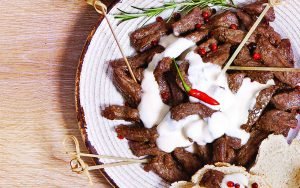 Prato de iscas de filé mignon com molho de queijo, decorado com pimenta rosa e pimenta dedo-de-moça