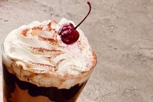 Copo de gin macchiato coberto com chantilly e cereja