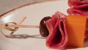 Espetos de queijo cheddar e salame, servidos em um prato.