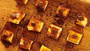 Cubos de queijo coalho dourados cobertos com melaço de café em uma tábua de madeira