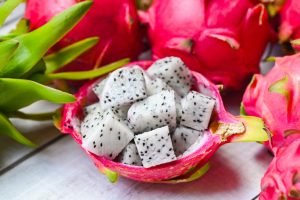 Pitaya branca cortada mostrando polpa clara com sementes pretas dentro de casca rosa vibrante, cercada por frutas inteiras