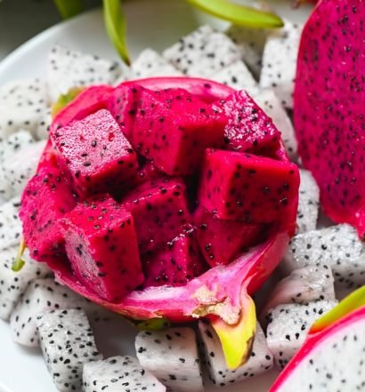 Pitayas vermelha e branca cortadas em prato branco, mostrando a polpa com sementes pretas da fruta versátil e saborosa