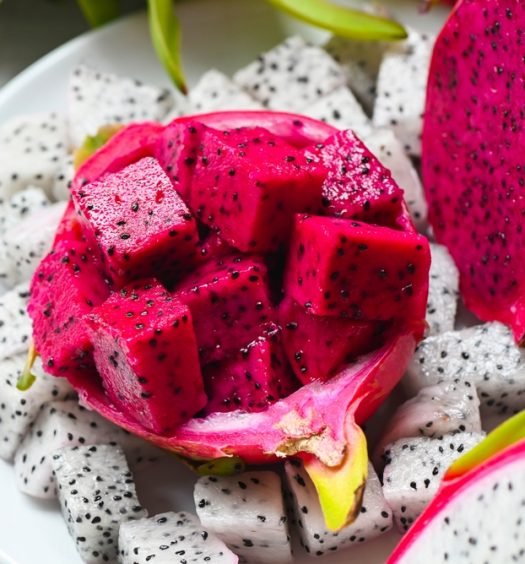 Pitayas vermelha e branca cortadas em prato branco, mostrando a polpa com sementes pretas da fruta versátil e saborosa