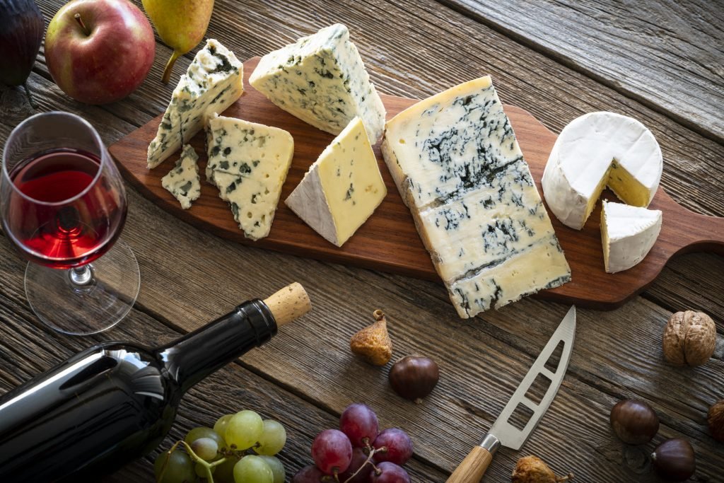 Tábuas de queijos finos acompanhados de vinho tinto, uvas, nozes e maçãs