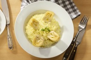 Risoto cremoso de coração de alcachofra em prato branco redondo, decorado com um pequeno ramo de manjericão
