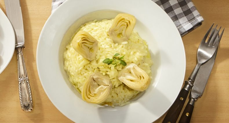 Risoto cremoso de coração de alcachofra em prato branco redondo, decorado com um pequeno ramo de manjericão