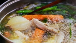 Caldo de mocotó com legumes, cebola, cenoura e verduras em uma panela.