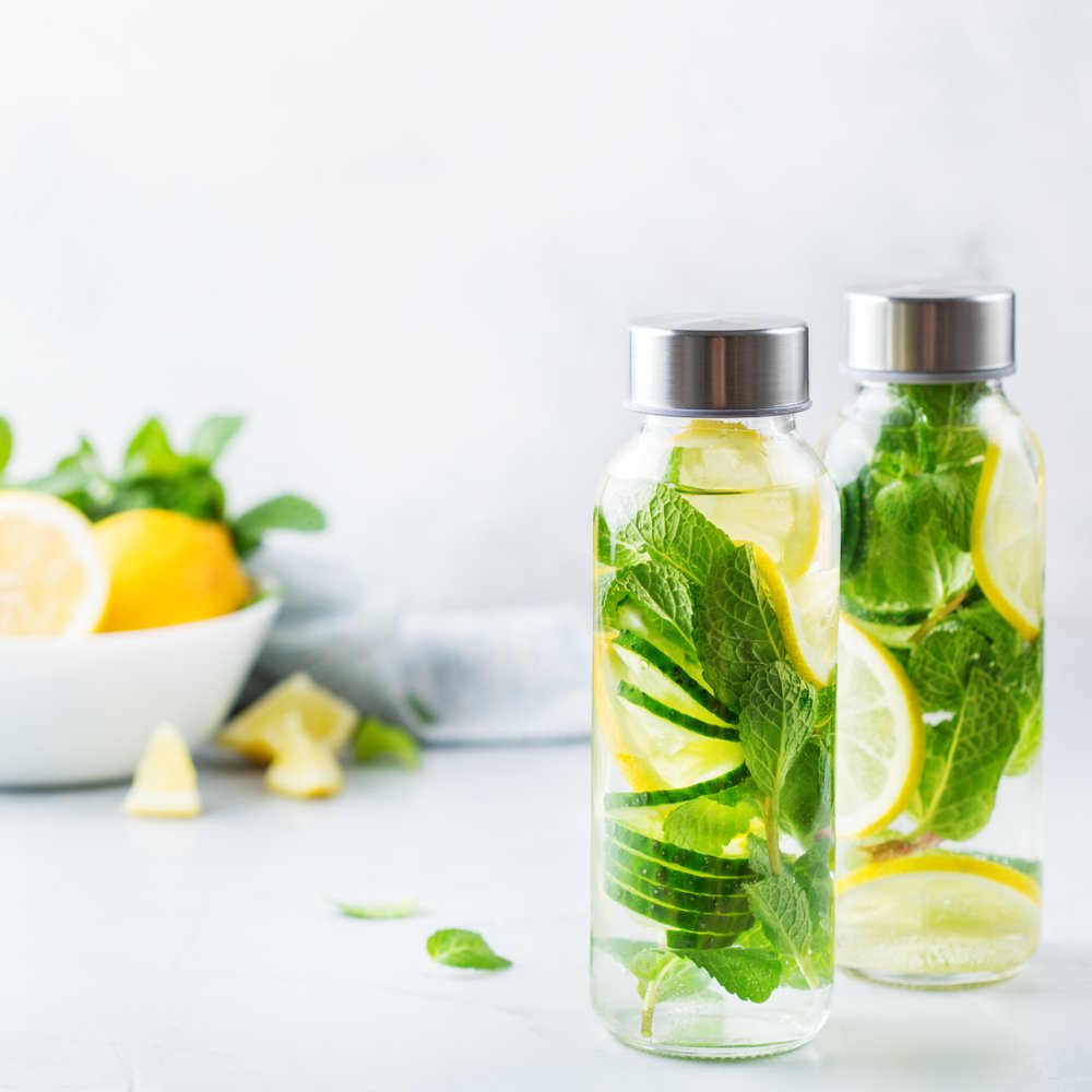 Água saborizada com limão e hortelã em garrafas de vidro com tampa de metal - bebida refrescante e natural para piquenique ao ar livre