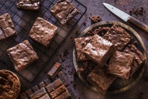 Brownies de chocolate caseiros cortados em quadrados, apresentados em grade de metal e prato rústico, com ingredientes de chocolate ao fundo - sobremesa decadente para piquenique