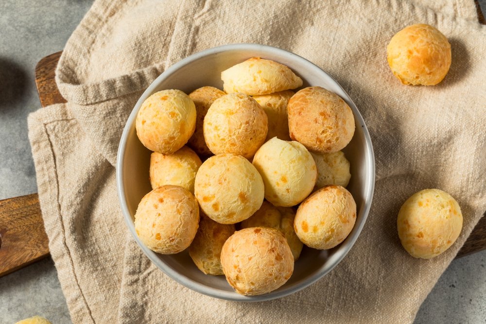 Tigela com pãezinhos de queijo dourados e crocantes, sobre toalha de linho, como acompanhamento perfeito para piquenique
