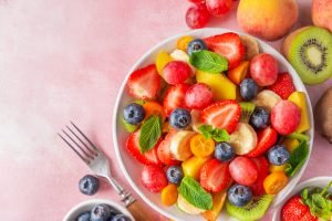 Salada de frutas colorida com morangos, mirtilos, kiwi, melancia e laranja em tigela branca, decorada com folhas de hortelã fresca - sobremesa refrescante para piquenique
