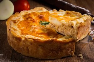 Torta de frango com massa folhada dourada e recheio cremoso, acompanhada de tomate, alface e alecrim - opção prática para piquenique