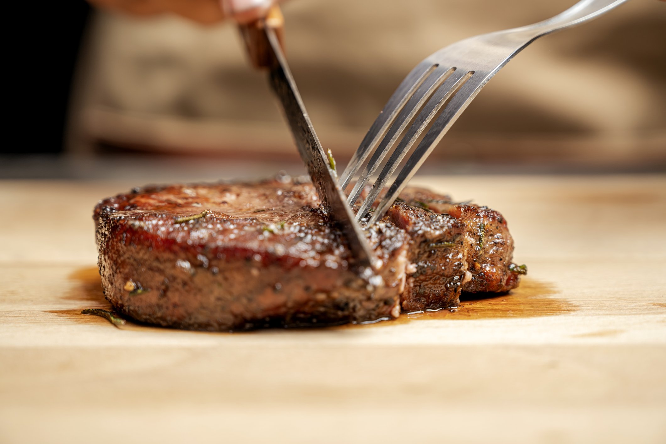  Carne suculenta sendo cortada com garfo e faca.