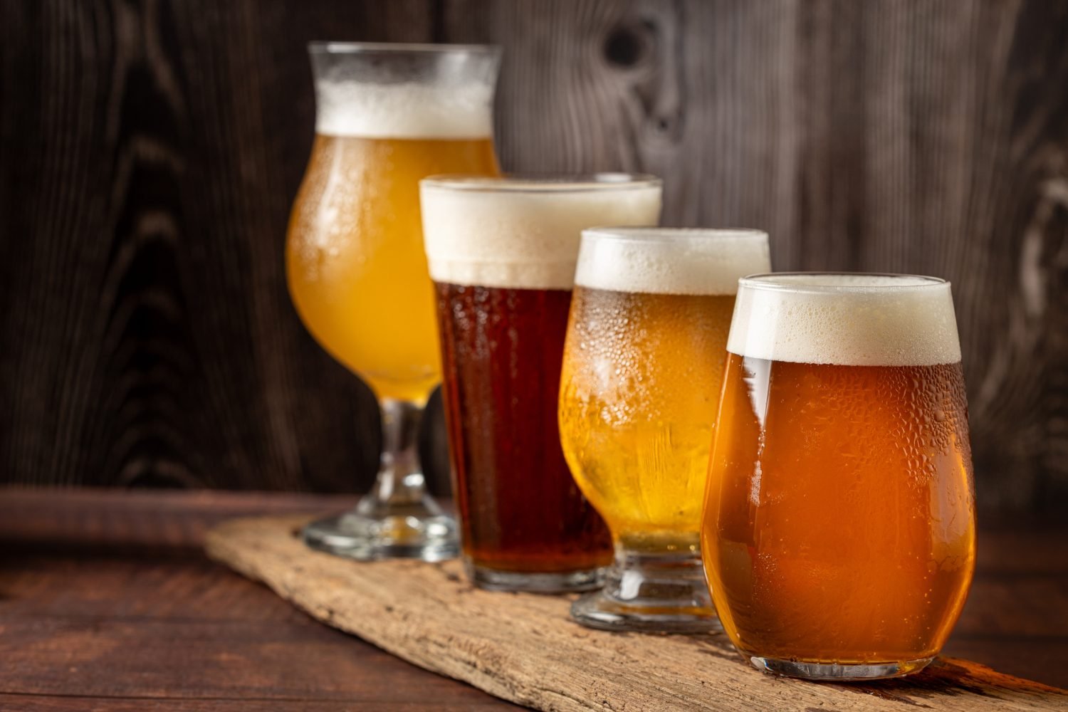 quatro copos de cerveja diferentes em uma mesa de madeira.