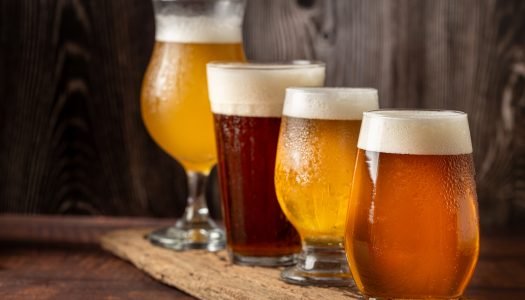 quatro copos de cerveja diferentes em uma mesa de madeira.