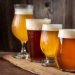quatro copos de cerveja diferentes em uma mesa de madeira.