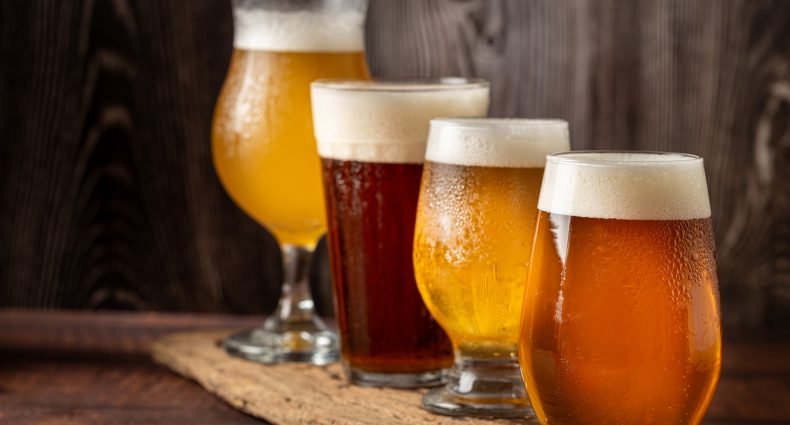 quatro copos de cerveja diferentes em uma mesa de madeira.