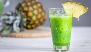 Suco detox verde servido em um copo com uma fatia de abacaxi na borda