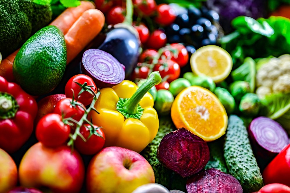 Frutas e vegetais coloridos — abacate, cenoura, tomate, mirtilo, laranja, cebola roxa, brócolis e outras hortaliças frescas representando o grupo de frutas e vegetais da pirâmide alimentar.