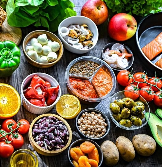 Variedade de alimentos frescos da pirâmide alimentar — vegetais, frutas, proteínas e grãos organizados sobre superfície escura, representando uma alimentação equilibrada.