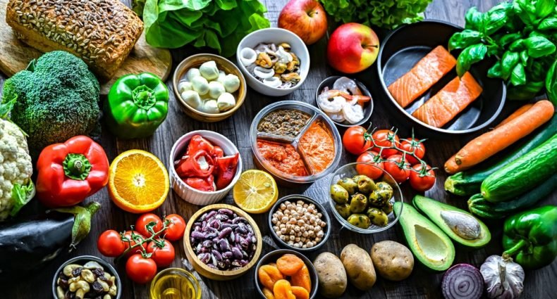 Variedade de alimentos frescos da pirâmide alimentar — vegetais, frutas, proteínas e grãos organizados sobre superfície escura, representando uma alimentação equilibrada.