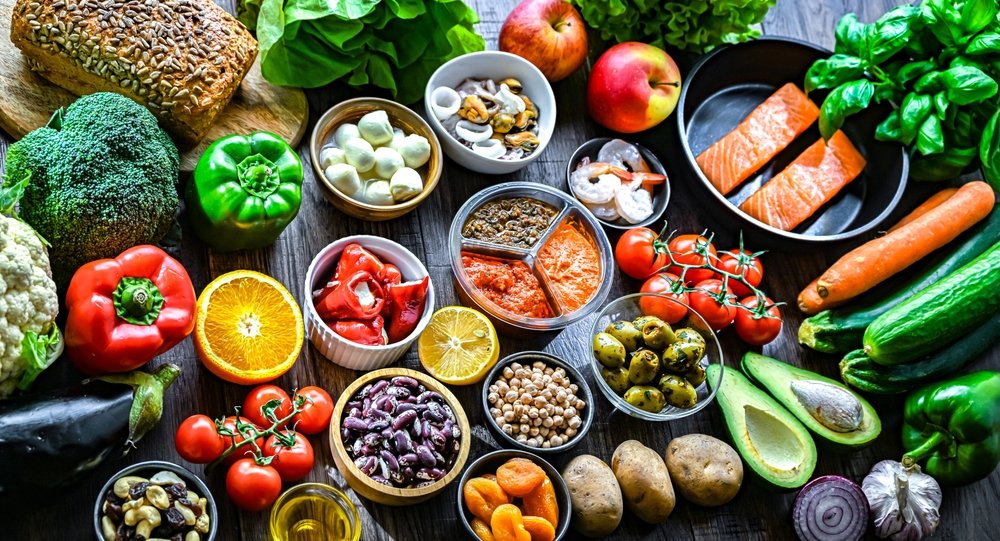 Variedade de alimentos frescos da pirâmide alimentar — vegetais, frutas, proteínas e grãos organizados sobre superfície escura, representando uma alimentação equilibrada.