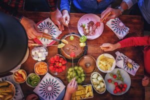 Grupo de amigos fazendo fondue de chocolate com frutas.