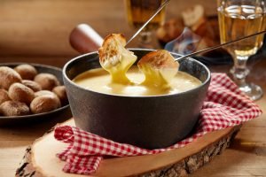 Fondue de queijo derretido com pão crocante ao fundo.