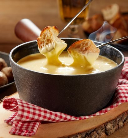 Fondue de queijo derretido com pão crocante ao fundo.