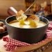 Fondue de queijo derretido com pão crocante ao fundo.