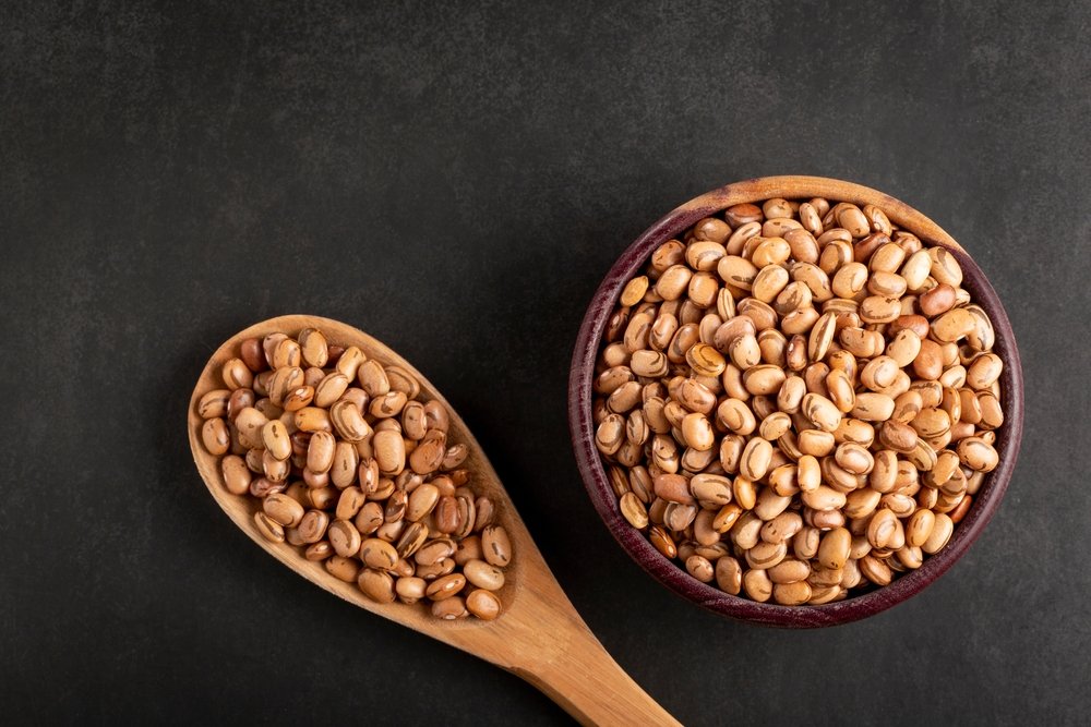 Colher de madeira e tigela cheia de feijão-carioca cru sobre fundo escuro, destacando o tipo de feijão mais consumido no Brasil