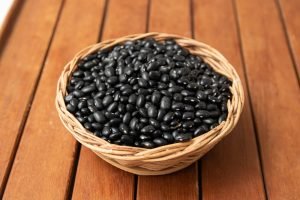 Cesta de palha cheia de feijão-preto cru sobre superfície de madeira, ilustrando tipo de feijão usado na feijoada
