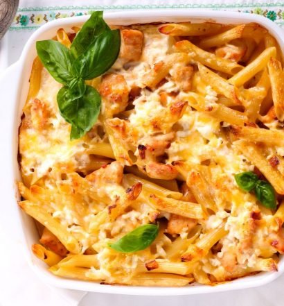 Massa penne gratinado com queijo Kroon Gouda em travessa branca, decorada com folhas de manjericão fresco.