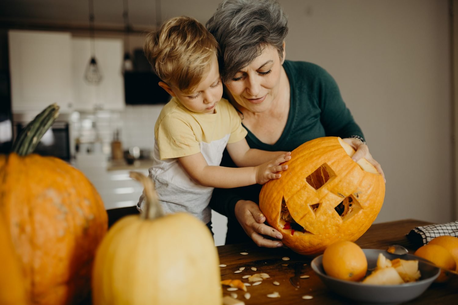 Adulto e criança decorando abóbora Jack-o'-lantern na cozinha para festa de Halloween