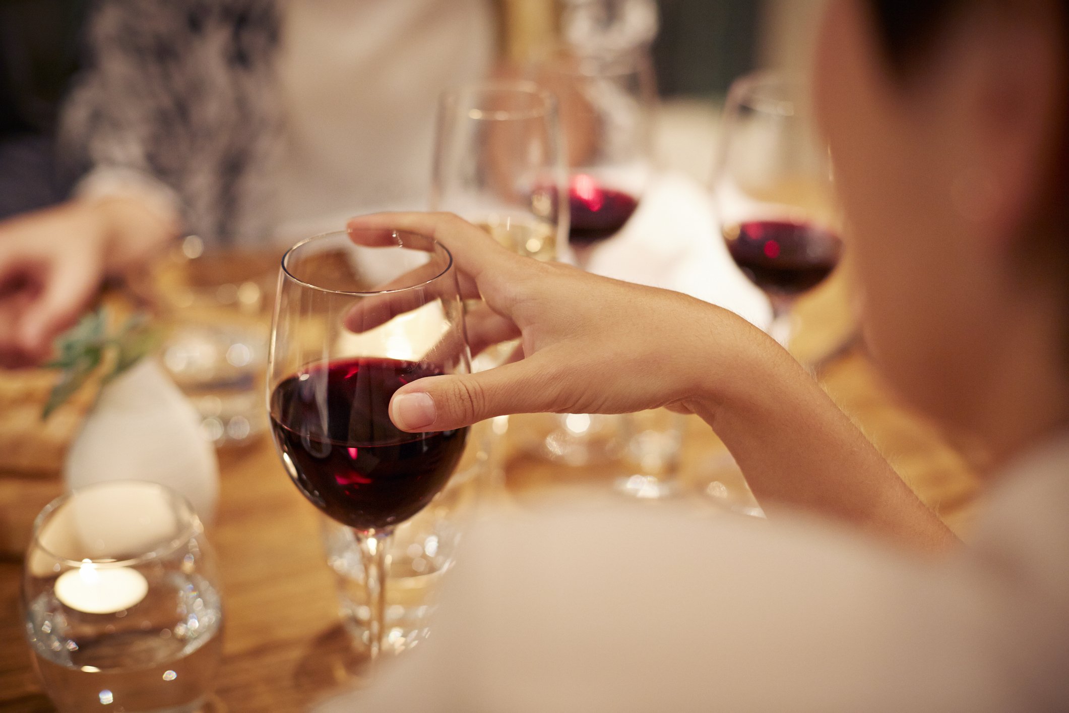 Mulher segurando taça de vinho tinto em jantar com amigos