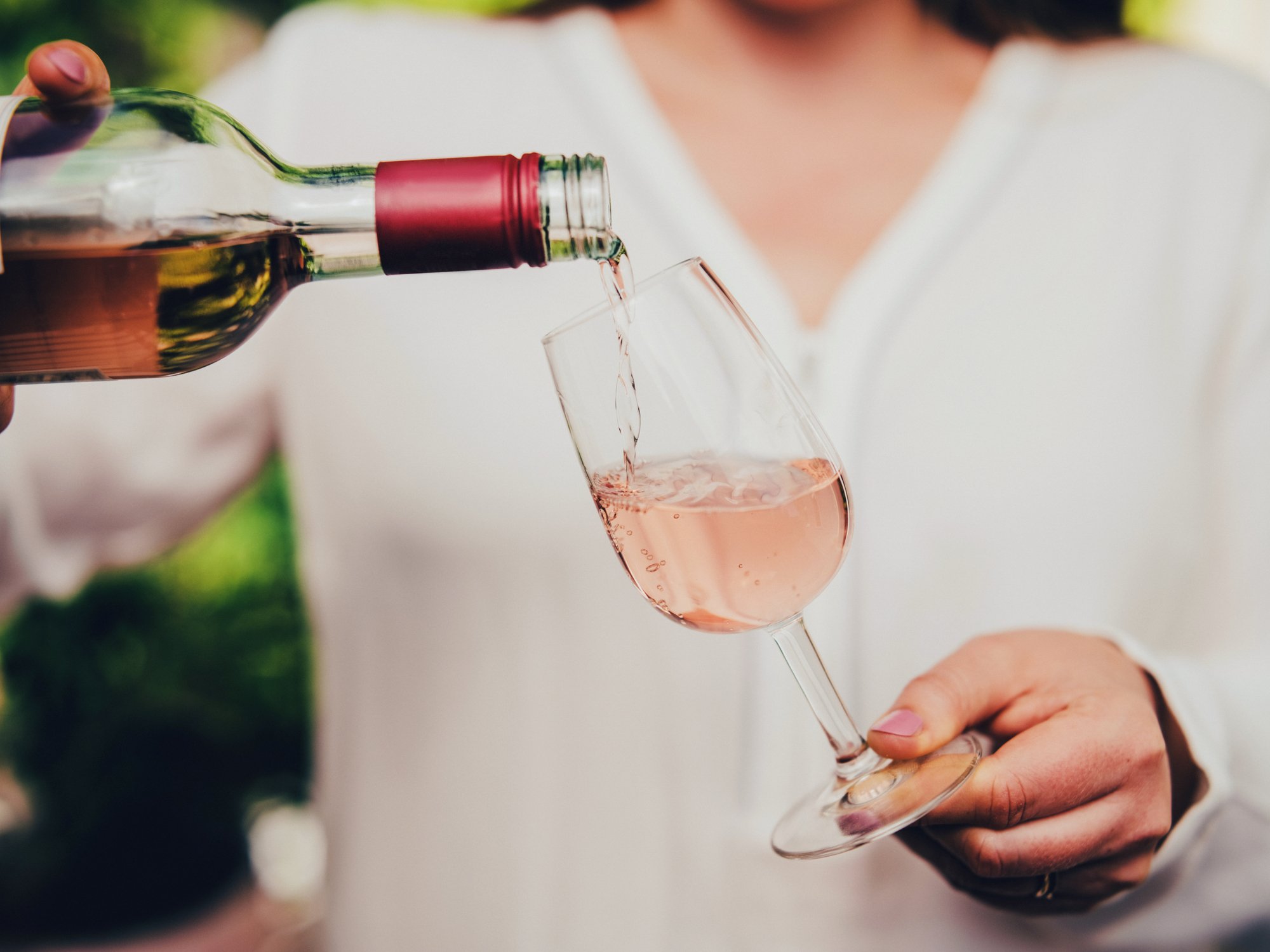 Mão servindo taça de vinho rosé; consumo moderado associado à melhora da função cerebral e da memória.