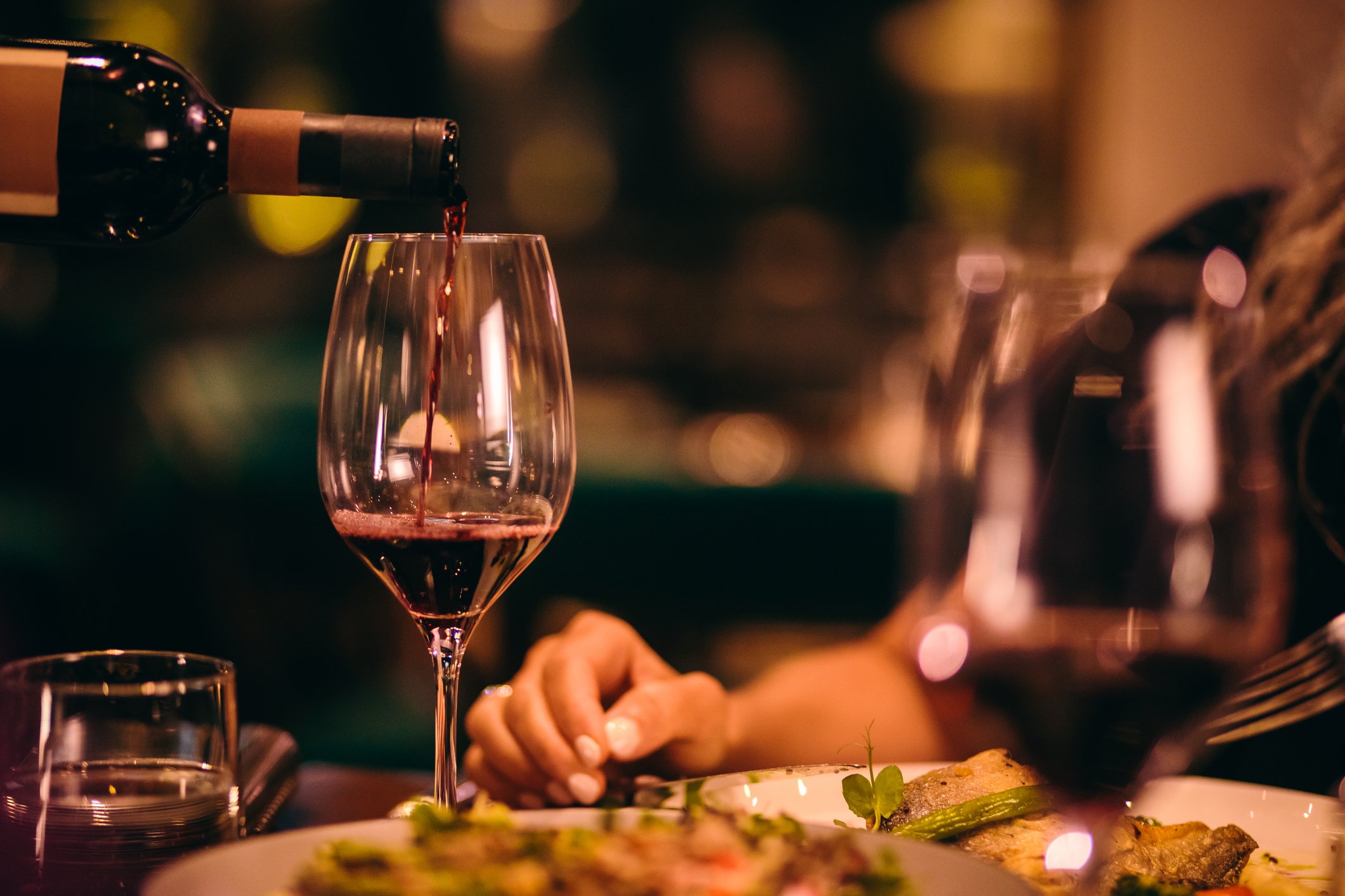 Vinho tinto sendo servido ao lado de um prato em jantar íntimo