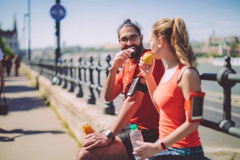 Casal sentado comendo fruta e barra de proteína após corrida ou treino