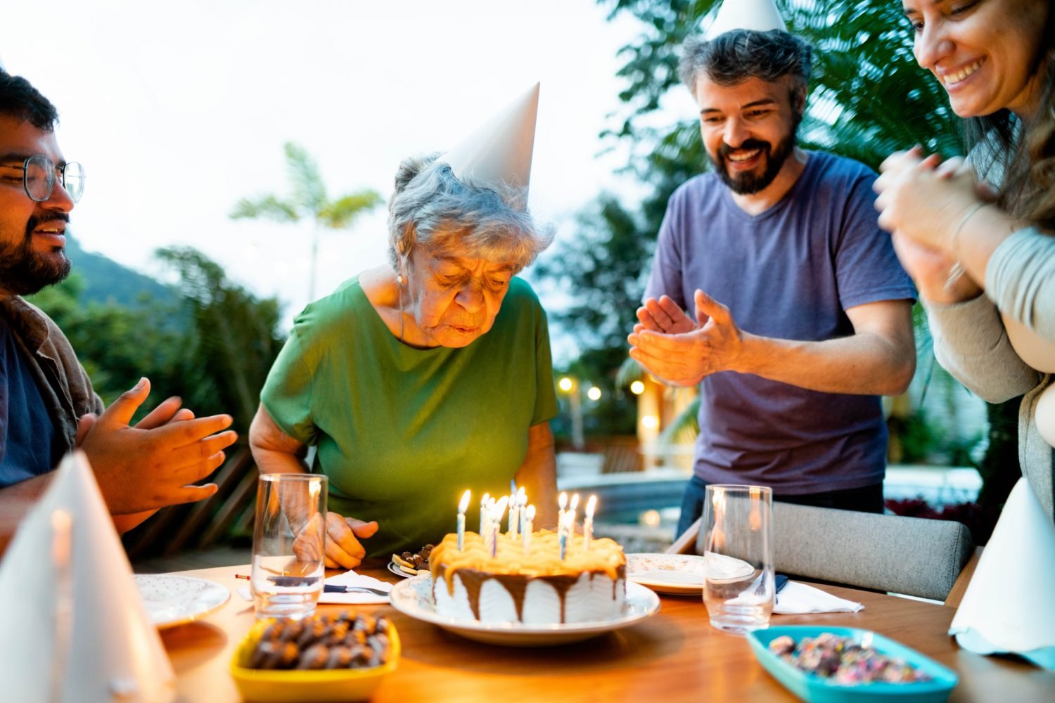 Idosa soprando velas de aniversário cercada por amigos e familiares