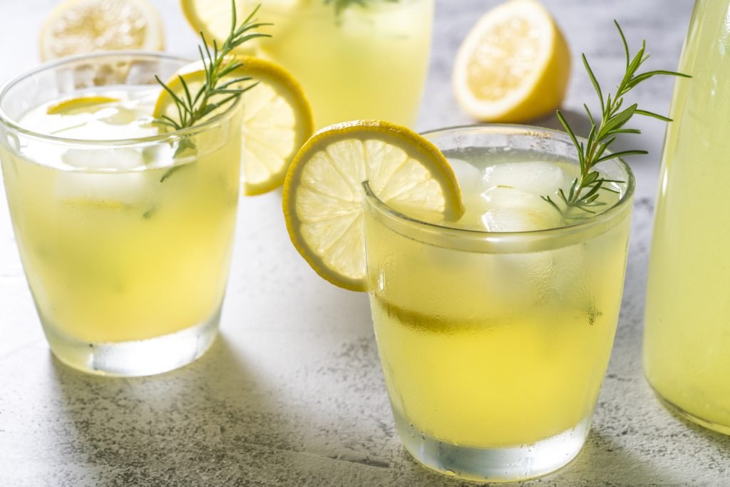 Copos baixos com drinque amarelo claro, decorados com fatias de limão e ramos de alecrim fresco