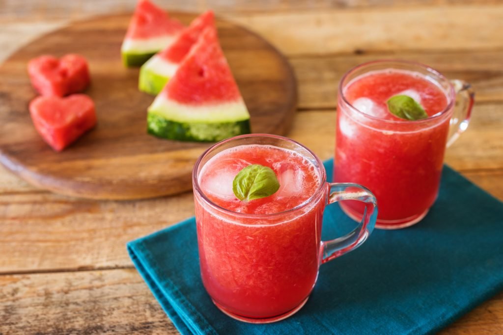 Copos com drinque rosa de melancia e maçã, decorado com fatias de frutas.