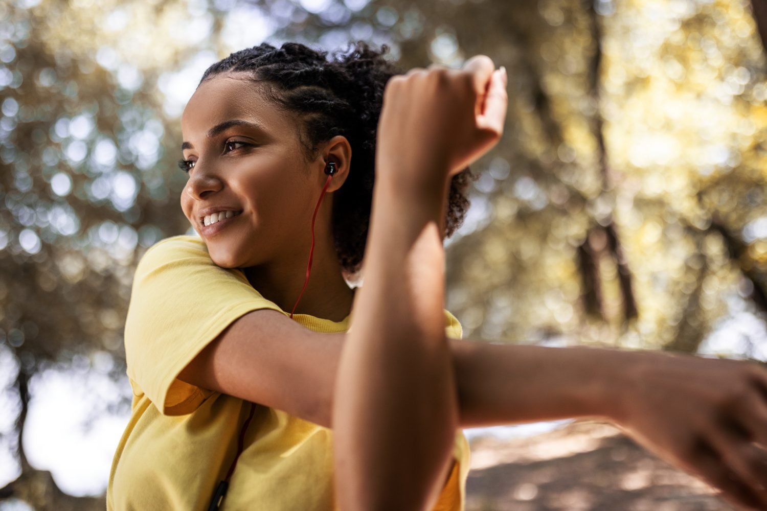 Mulher jovem sorrindo e alongando-se ao ar livre com fones de ouvido