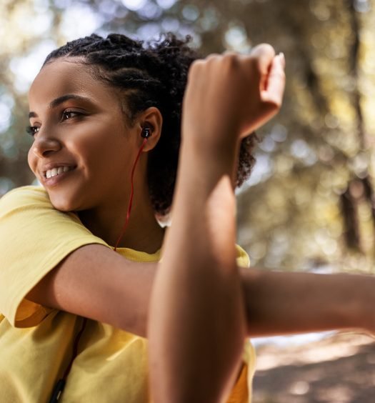 Mulher jovem sorrindo e alongando-se ao ar livre com fones de ouvido
