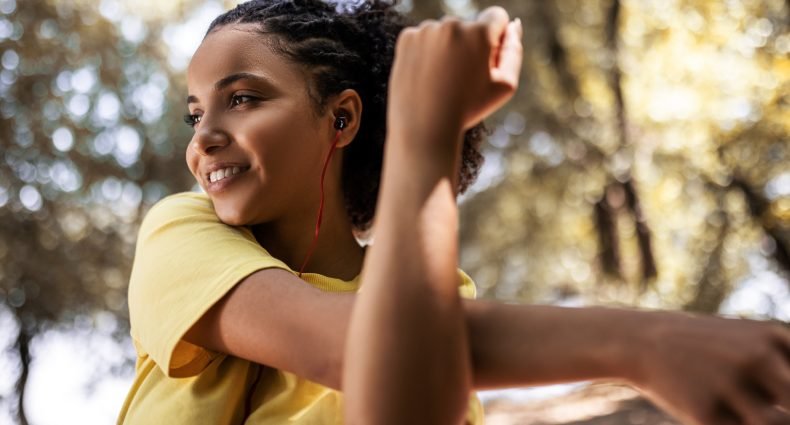 Mulher jovem sorrindo e alongando-se ao ar livre com fones de ouvido