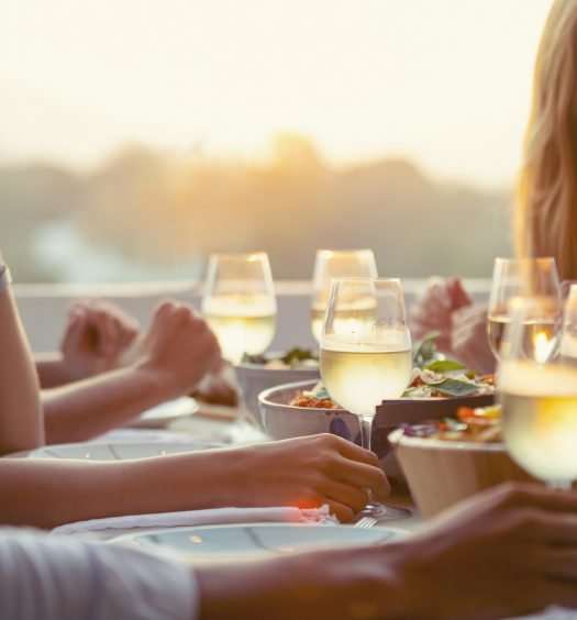 Pessoas felizes compartilhando uma refeição ao ar livre com drinks e pratos leves