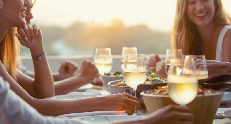 Pessoas felizes compartilhando uma refeição ao ar livre com drinks e pratos leves