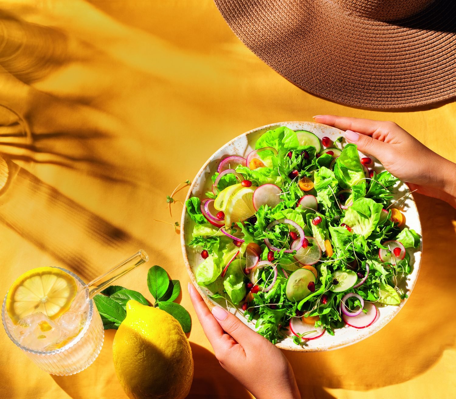 Prato de salada fresca com folhas verdes, rabanetes, tomates cereja e fatias de limão sobre uma toalha amarela