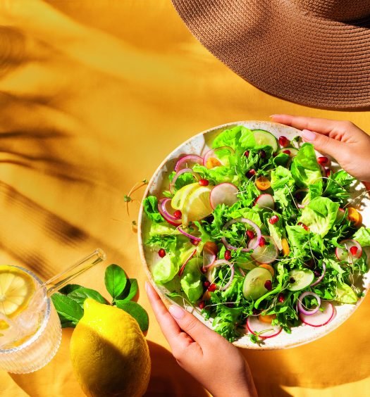 Prato de salada fresca com folhas verdes, rabanetes, tomates cereja e fatias de limão sobre uma toalha amarela